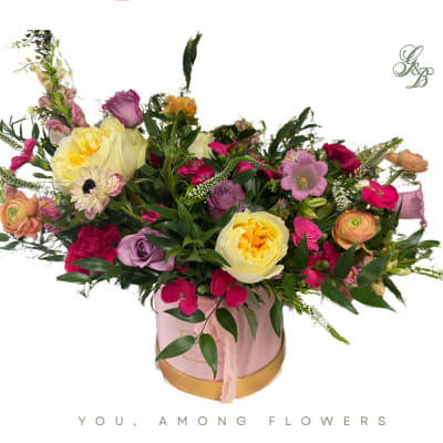 Mixed pink, yellow, and purple flowers arranged in a pink round box