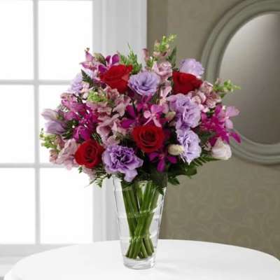 Bouquet of red, pink, and lavender flowers in a clear glass vase