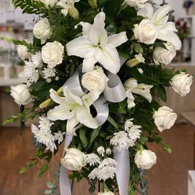 White roses and lilies arranged on a standing spray with ribbon.