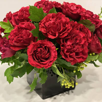 Red rose bouquet in a black square vase with green foliage