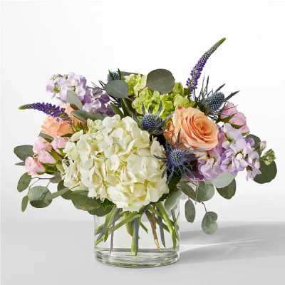 Low glass vase of white hydrangeas, peach roses, and pastel blooms with blue accents.