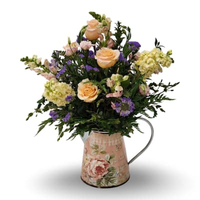 Peach roses and purple flowers arranged in a floral metal pitcher