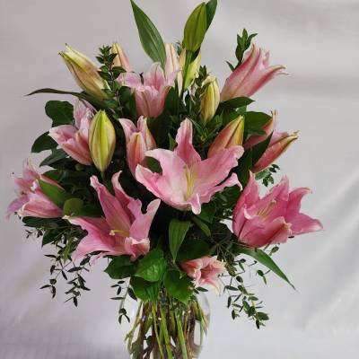 Pink lilies arranged in a clear glass vase with greenery