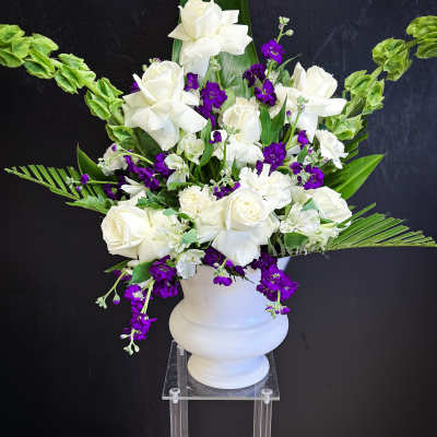 White roses and purple flowers arranged in a white urn vase