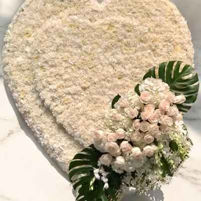 Heart-shaped white floral arrangement with pale pink roses and tropical leaves