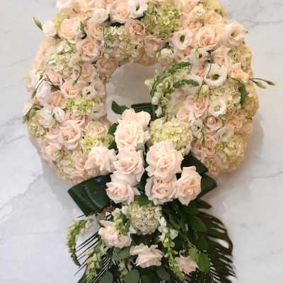 Large floral wreath of pale pink roses and cream blooms with dark green ribbon