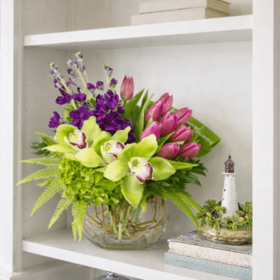 Bouquet of green orchids, pink tulips, and purple flowers in a glass vase