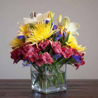 Mixed bouquet of lilies, alstroemeria, and yellow spider mums in a glass vase