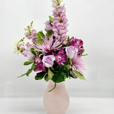Pink and lavender flowers arranged in a pale pink vase