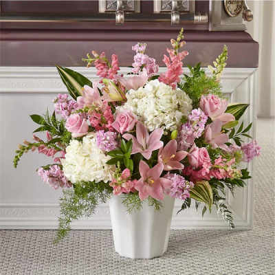 Tall arrangement of pink lilies, roses, and white hydrangeas in a white vase