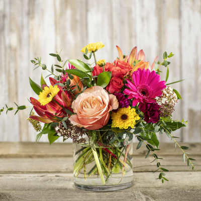 Mixed bouquet of roses, gerbera daisies, and other flowers in a glass vase