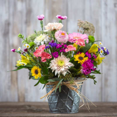 Mixed bouquet of colorful flowers in a metal vase with a raffia bow