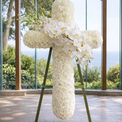 White floral cross on an easel with orchids and clustered blooms