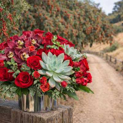 Red roses and orchids arranged with succulents in a silver vase