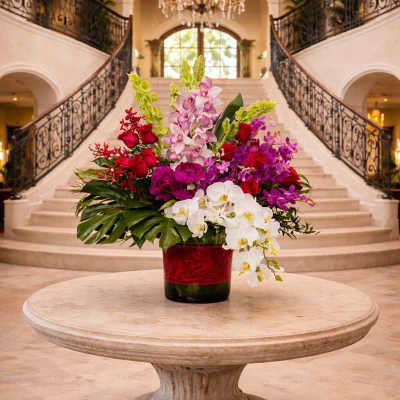 Large mixed orchid arrangement in a red vase on a round table