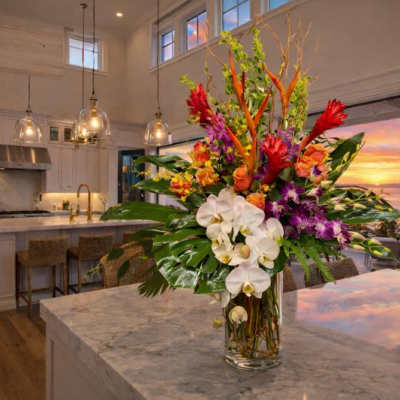 Tall tropical bouquet with white orchids and red-orange flowers in a glass vase