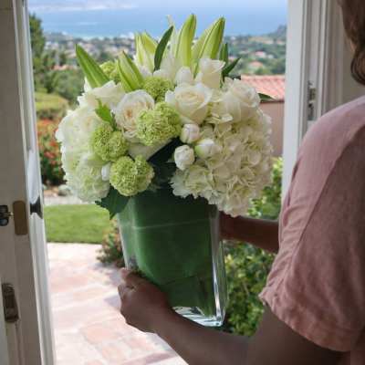 White floral arrangement in a clear glass vase being held at a doorway