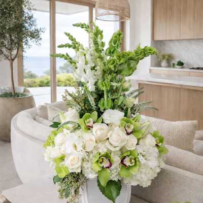 White and green floral arrangement in a white vase on a table