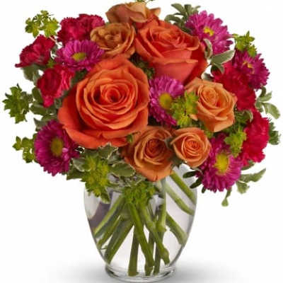 Orange roses and magenta daisies in a clear glass vase
