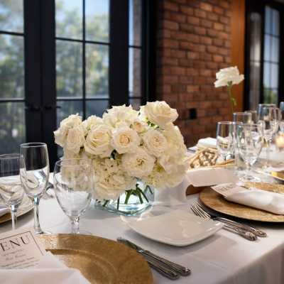 White floral centerpiece on a set dining table with glassware and gold chargers