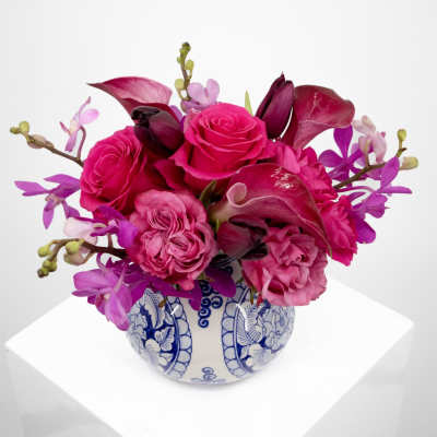 Pink roses and orchids arranged in a blue-and-white ceramic vase.
