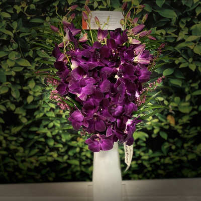 Purple orchid arrangement in a tall white vase