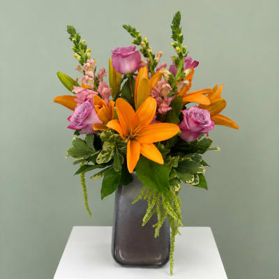 Orange lilies and pink roses in a dark vase