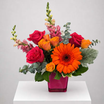 Bouquet of red and orange roses with a bright orange gerbera in a pink vase