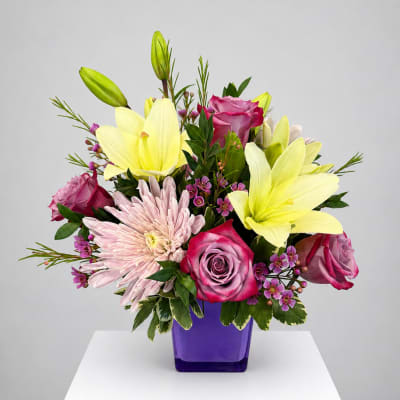 Bouquet of yellow lilies, pink roses, and pale pink chrysanthemums in a purple vase