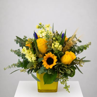 Yellow roses and a sunflower in a yellow vase with mixed greenery