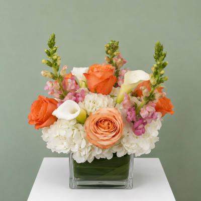 Orange roses and white calla lilies in a square glass vase