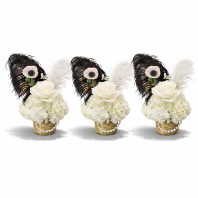 Three white floral arrangements in woven baskets with black and white feathers