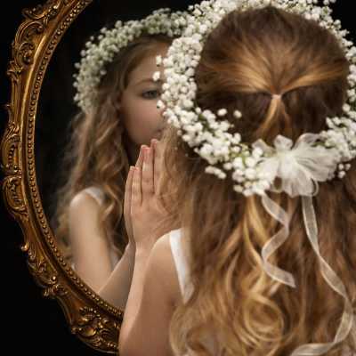 Girl wearing a white flower crown and looking into an ornate mirror