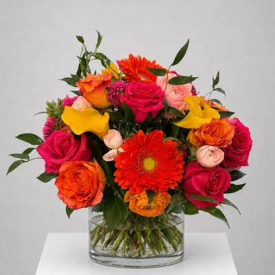 Bright mixed bouquet of roses, gerbera daisies, and calla lilies in a glass vase