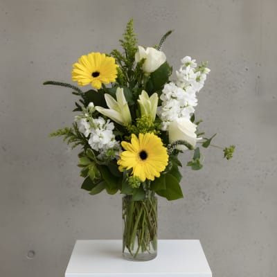 Yellow gerbera daisies and white lilies in a clear glass vase
