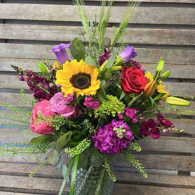 Mixed bouquet in a glass vase with a sunflower, roses, lilies, and purple blooms