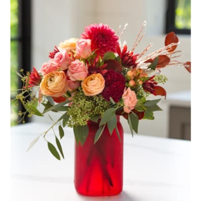 Mixed red and peach flower arrangement with roses and ranunculus in a red glass vase
