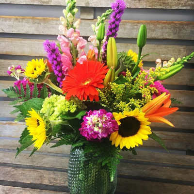 Colorful mixed bouquet in a green glass vase with sunflowers and lilies
