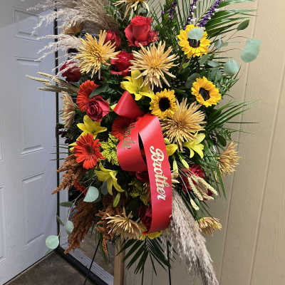 Tall standing floral spray with red and yellow flowers and a red ribbon