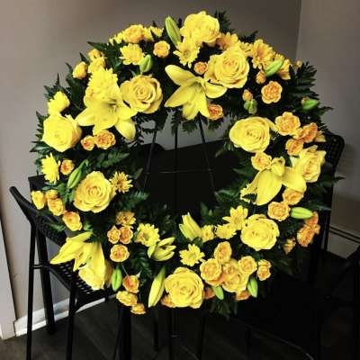 Yellow floral wreath with roses, lilies, and daisies on a stand