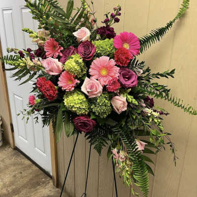 Standing floral spray with pink and burgundy blooms on a black easel