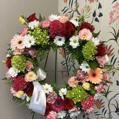 Heart-shaped floral wreath with roses, daisies, and carnations on an easel