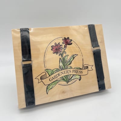 Wooden gardener’s press with floral illustration and two black straps