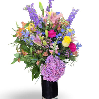 Colorful mixed bouquet in a black vase with lilies, roses, and purple blooms