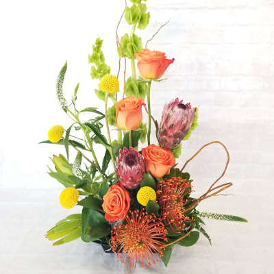 Tall mixed bouquet with orange roses, protea, and yellow accents in a vase