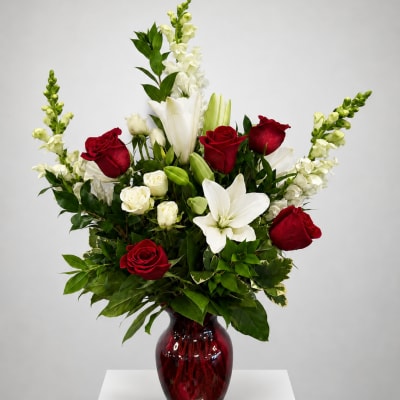 Red and white floral arrangement in a red glass vase