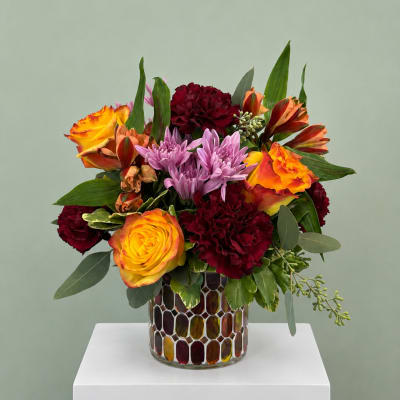 Mixed bouquet of orange roses, purple chrysanthemums, and burgundy carnations in a mosaic vase