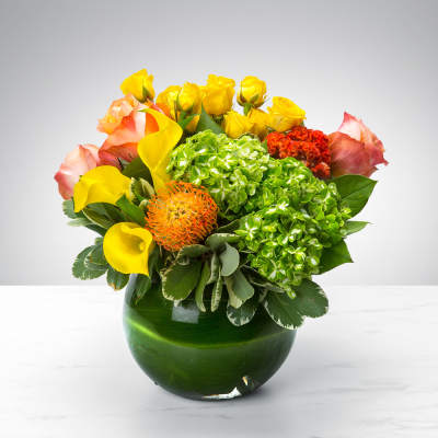 Bouquet of yellow roses, pink roses, calla lilies, and green hydrangeas in a green vase