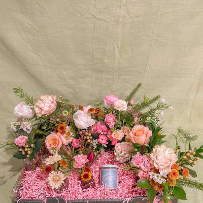 Mixed pink and peach flower arrangement in a gift box with a small candle