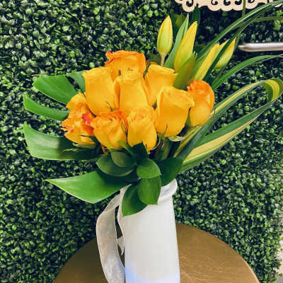 Yellow and orange roses in a white vase with a silver ribbon
